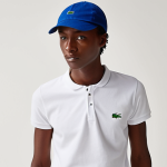 A gender-neutral individual effortlessly sporting a classic Lacoste tennis cap, showcasing its timeless and minimalist design. The cap seamlessly complements diverse outfits, from a casual T-shirt and jeans to a polo shirt, embodying versatile, understated sophistication in various everyday settings. The iconic small alligator logo is subtly visible, adding to its classic charm.